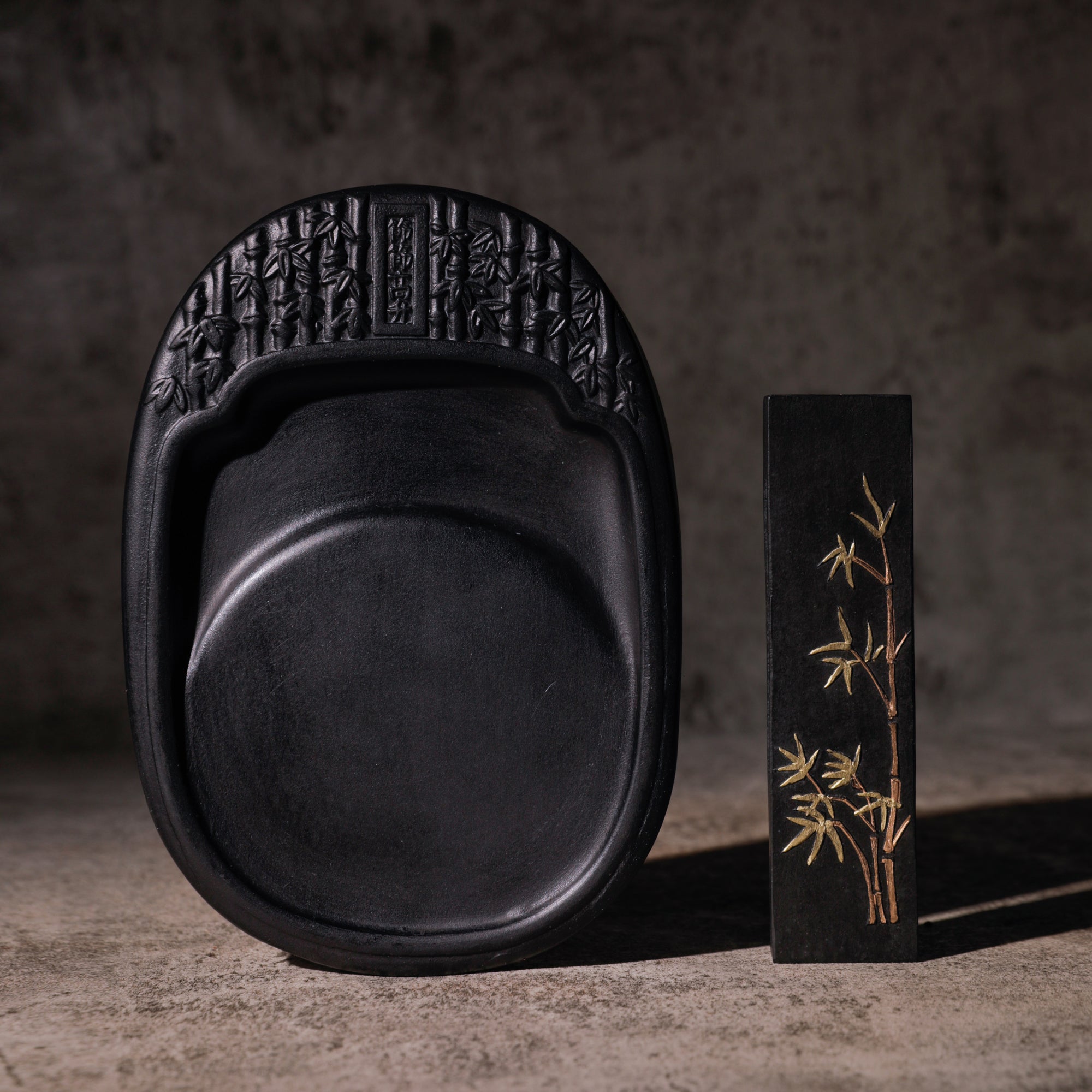 Black Chinese ink stick with golden bamboo print standing next to a black stone-made brush-painting ink slab