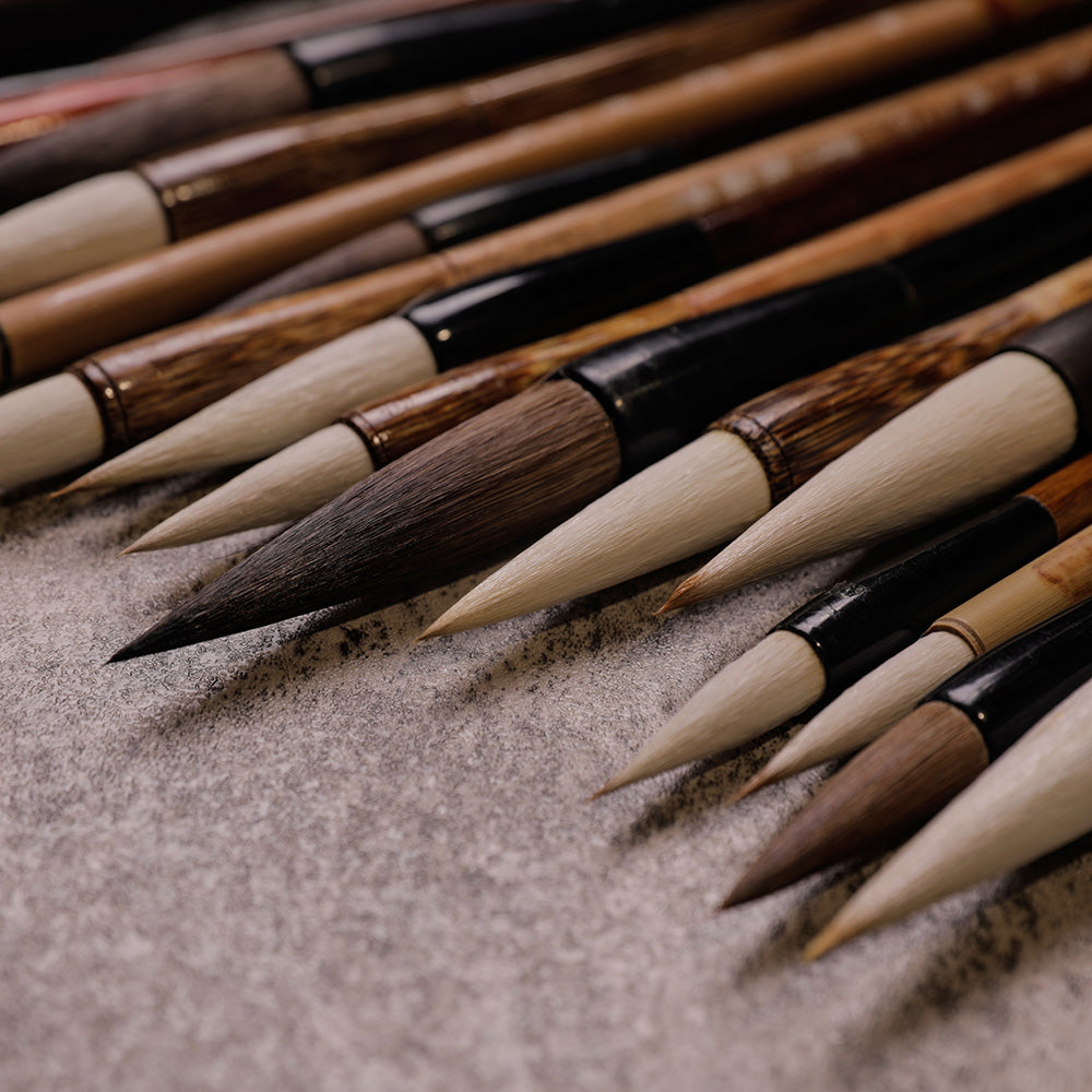 Closeup view of the tips of Chinese Calligraphy and Sumi Brushes with different tip sizes and beige bamboo handles and black wooden handles.