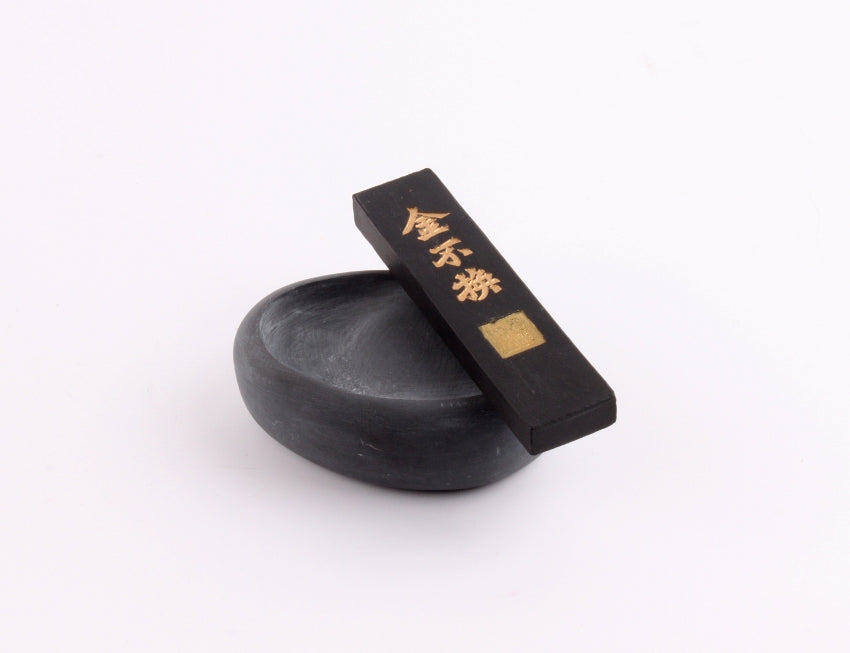 Chinese she yan ink stick shaped like a goose egg in grey color and coarse surface together with black ink stick with golden characters printed on top