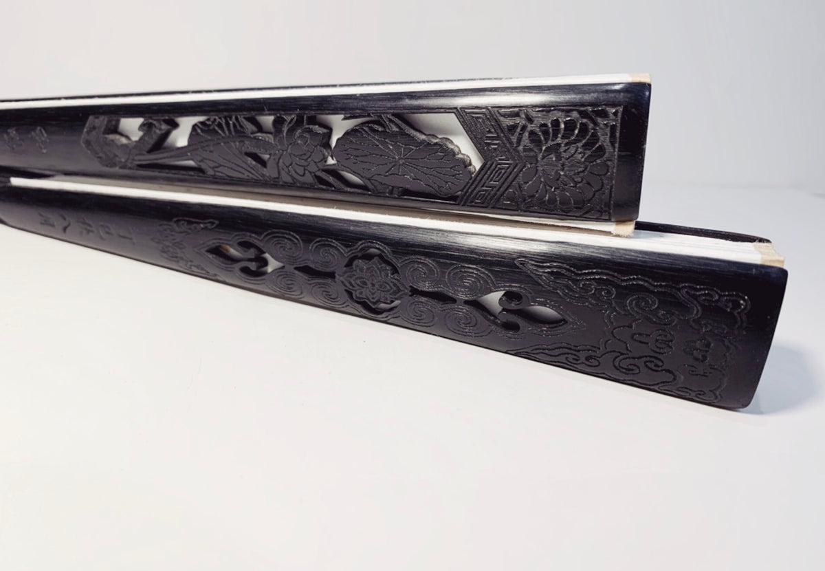 Oriental hand fans lying on the side showing the carving pattern on the handle made of dark Chinese wood.