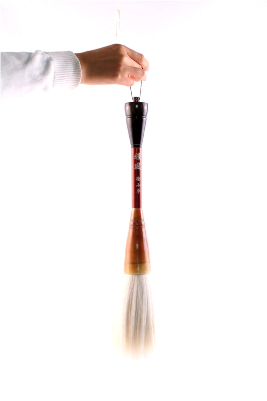 Very long Chinese brush made of redwood, water buffalo and goat hair bristles held on a stretched out human hand to show a size relation displaying how big this artist brush is.
