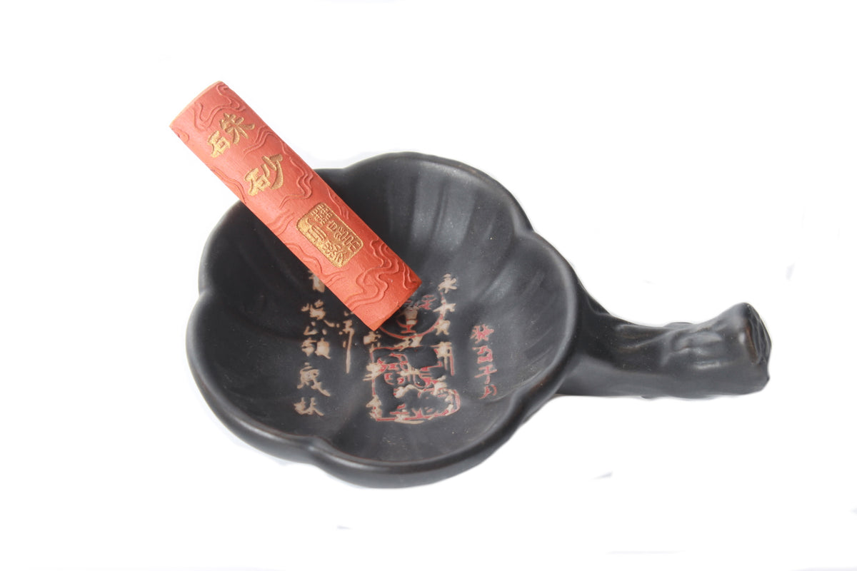 A black hand carved ceramic brush rest with a red ink stick rest on it. 