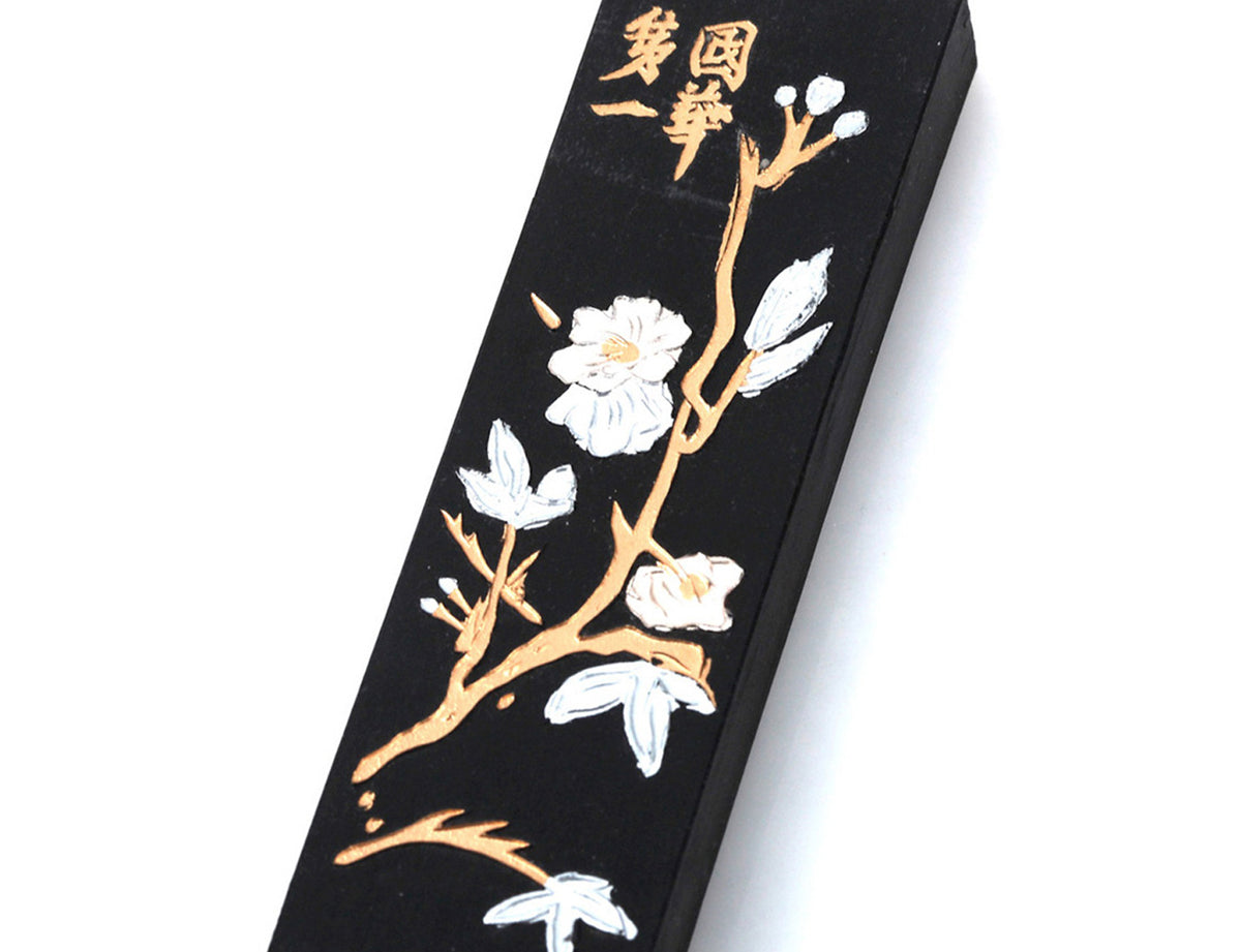 Black Japanes / Chinese ink stick for sumi and calligraphy, nicely decorated with white plum tree blossoms on golden branches and golden decorative Chinese lettering.