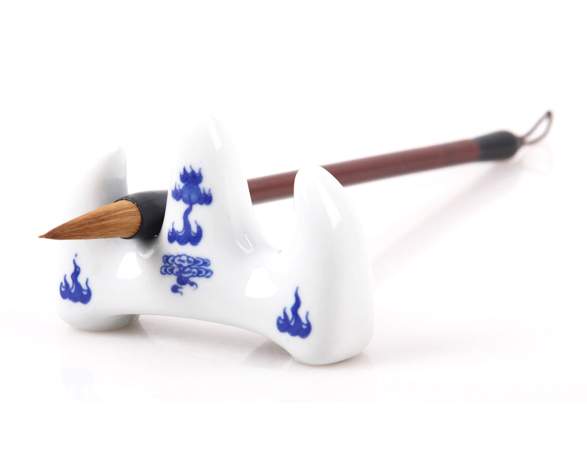 Typical traditional Chinese brush rack hand made of white ceramic with  blue decorative patterns of flames used in Sumi painting and calligraphy writing - picture showing one gongbi brush resting on the stand to display its usage
