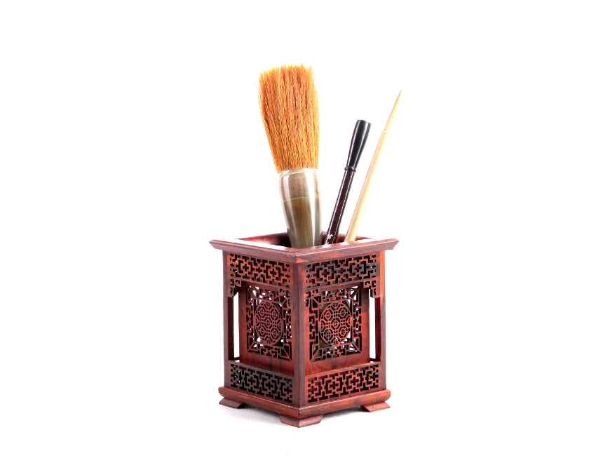 Display of Chinese brushes placed in a wooden relief-carved square brush holder used in oriental calligraphy and sumi.