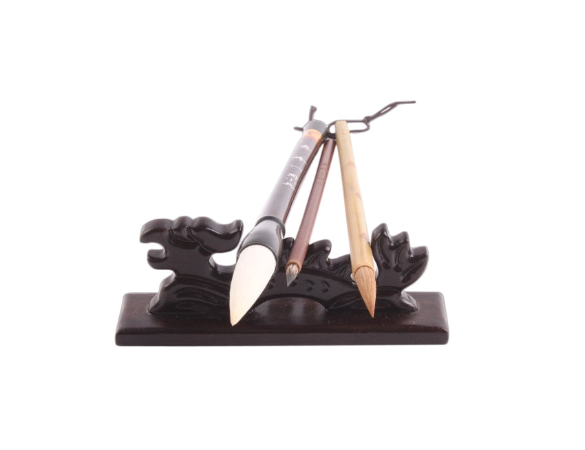 Traditional Chinese wooden brush rest in the shape of a little dragon taken from the front with 3 calligraphy brushes being positioned on it to display its usage
