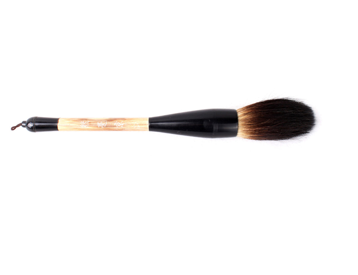 Thick tip dark goat hair bristles Chinese calligraphy and sumi brush lying flat on a surface and seen from the side. This brush has a hand-carved water buffalo and wooden handle and has similar characteristics as a more expensive bear hair brush.