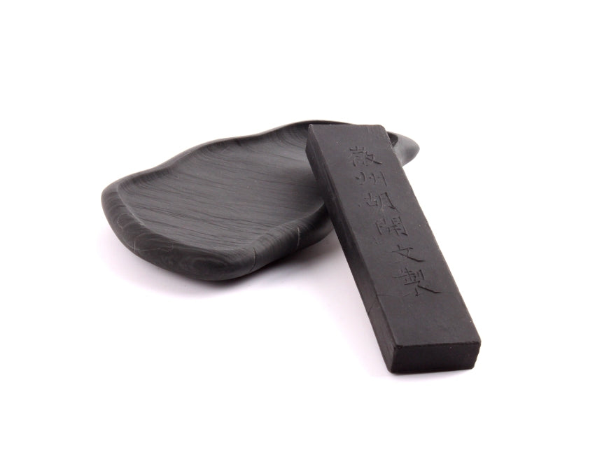 Assortment image of Oriental ink stone shaped like a leaf with leaf patterns on top and made of dark she yan stone together with a black small Chinese ink stick